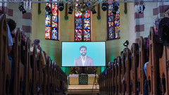 Vollbesetzter Gottesdienst mit einen Bildschirm im Altarraum
