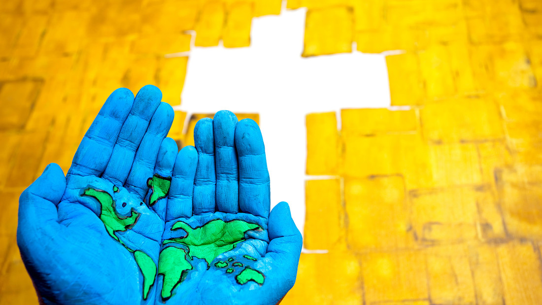 bemalte Hände mit einer Weltkarte vor einem Kreuz auf gelbem Hintergrund