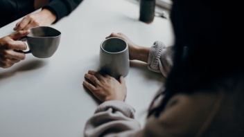 Auf einem Tisch sieht man zwei Hände, die je eine Kaffeetasse halten.