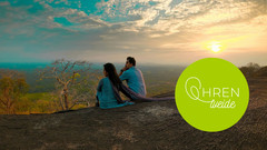 Paar sitzt auf Felsenformation, weite Landschaft mit Sonnenaufgang