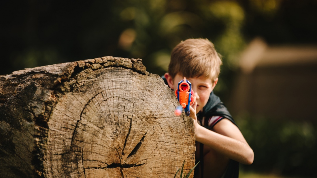 Ein Kind mit Plastikpistole versteckt sich hinter einem Baumstamm