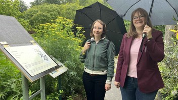 Die beiden jungen Theologinnen Alwine Schulze (links) und Aline Seidel stehen an einer Erklärtafel des Bibelpflanzenpfades in Marburg