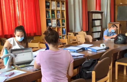 Schüler sitzen mit Maske auf Abstand am Tisch und lernen mit Computern