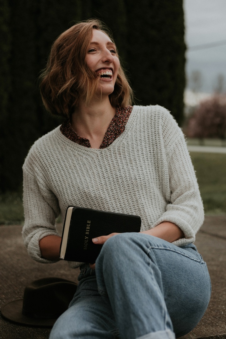 junge Frau hält Bibel während sie herzlich lacht