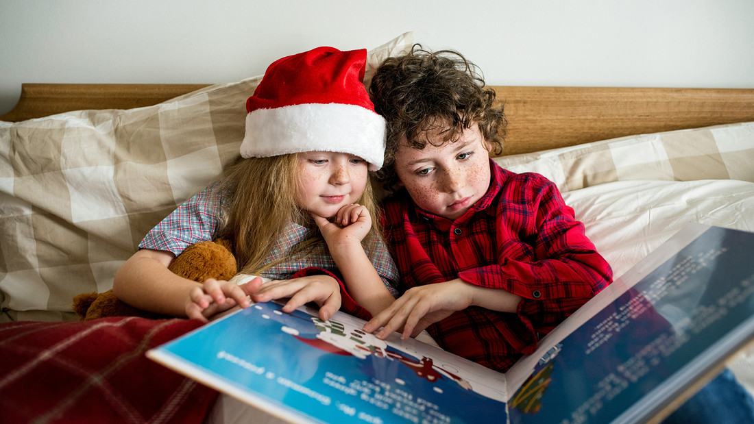 Zwei Kinder mit Weihnachtsbaummützen lesen ein Buch