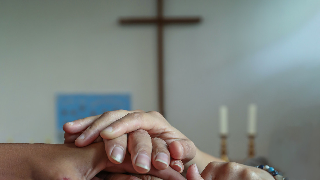Hände halten einander vor Kreuz in Kirche