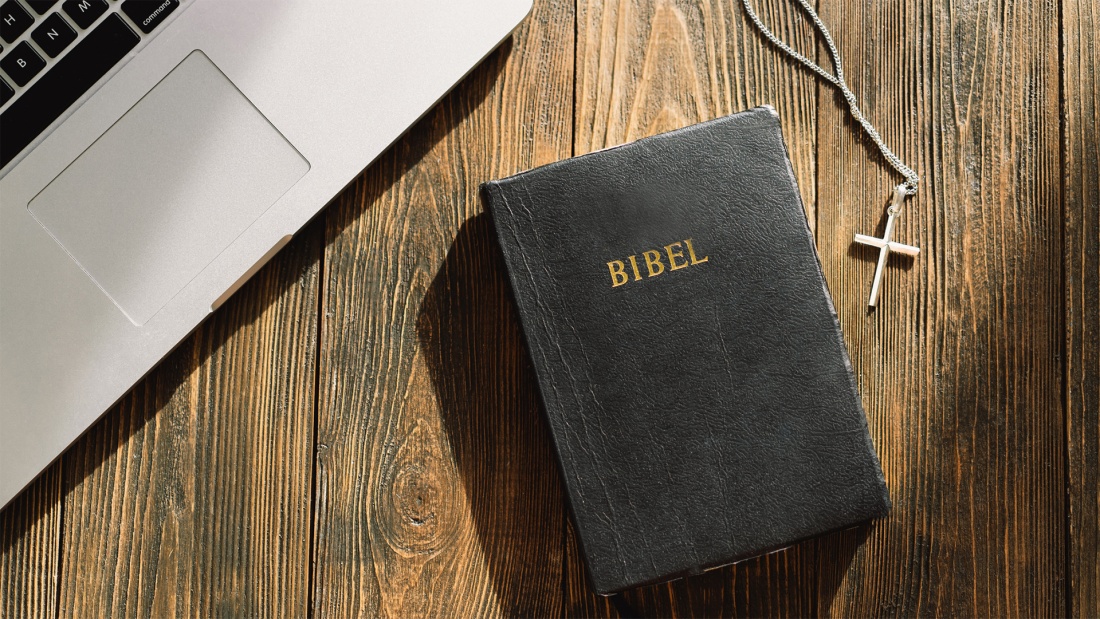 Bibel und Kreuz liegen neben Laptop