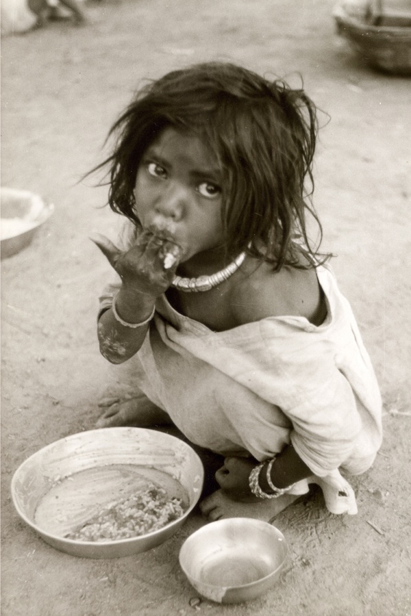 Ein indisches Kind sitzt auf der Erde vor einem Teller mit Essen.