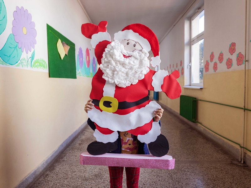 Schulkind hält in einer Schule einen großen, selbstgebastelten Weihnachtsmann in die Kamera 