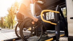Mann rollt mit Rollstuhl über Rampe in ein Fahrzeug