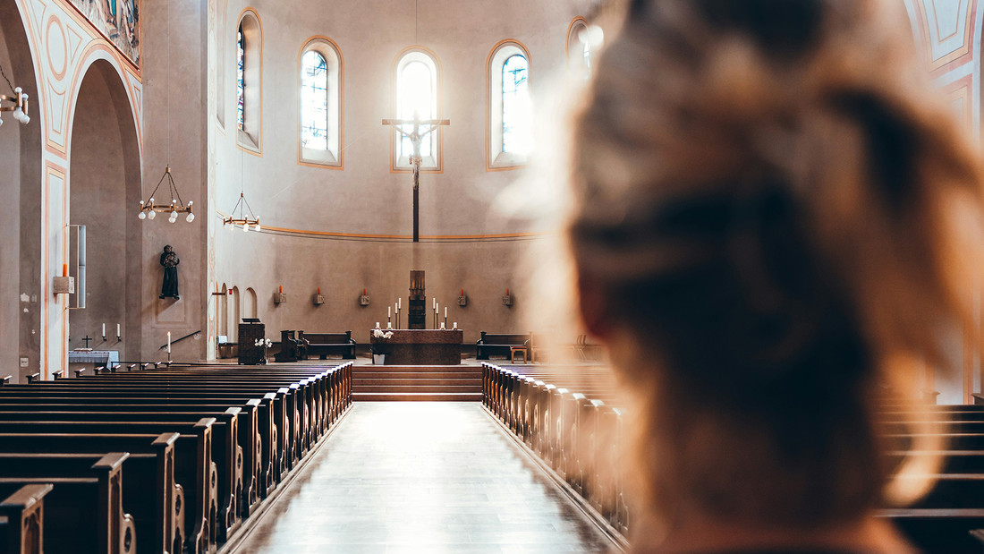 Junge Frau schaut  in einer Kirche in Richtung Altar