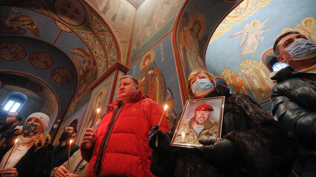 Menschen halten Kerzen und das Porträt eines Soldaten in einer Kathedrale in Kiew.