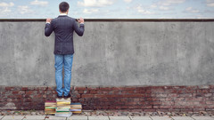 Mann steht auf Bücherstapel und schaut über Mauer