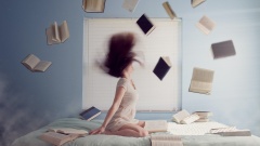 Frau wirft die Haare in die Luft auf einem Bett mit Büchern