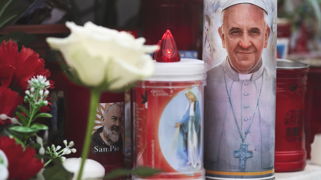 Blumen und Kerzen an der Statue von Papst Johannes Paul II. vor dem Eingang der Klinik