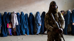 Ein Taliban-Kämpfer steht Wache vor wartenden Afghaninnen in Burkas