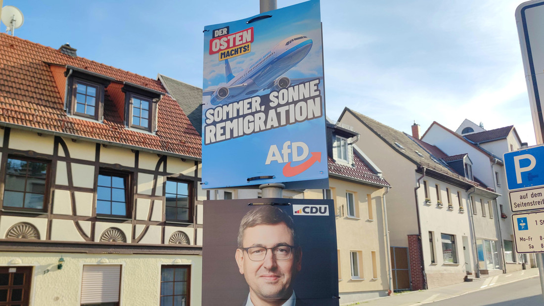 Wahlplakate zur Landtagswahl: AfD-Wahlplakat mit der Aufschrift "Der Osten machst - Sommer, Sonne, Remigration"; auf dem Flugzeug steht in kleiner Schrift "Abschiebe-Hansa"; darunter CDU-Plakat mit Christoph Zippel