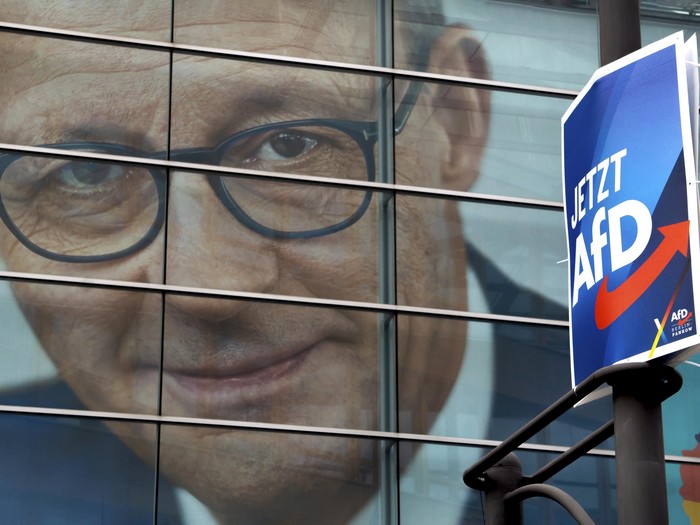 Ein Wahlplakat der AfD hängt vor einem übergroßen Wahlplakat der CDU, das Friedrich Merz im Portrait zeigt