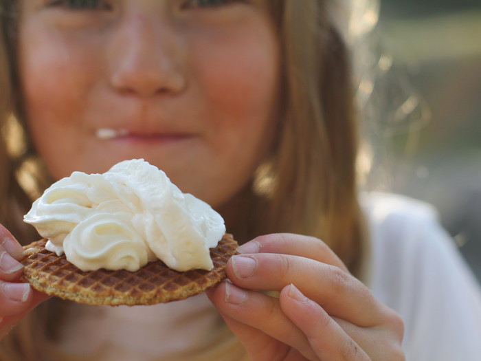 Junges Mädchen beißt in einer Waffel, die mit Sahne besprüht ist