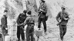 Altes Foto vom Berliner Mauerbau mit NVA-Soldaten, die mit Stacheldraht einen Zaun bauen.