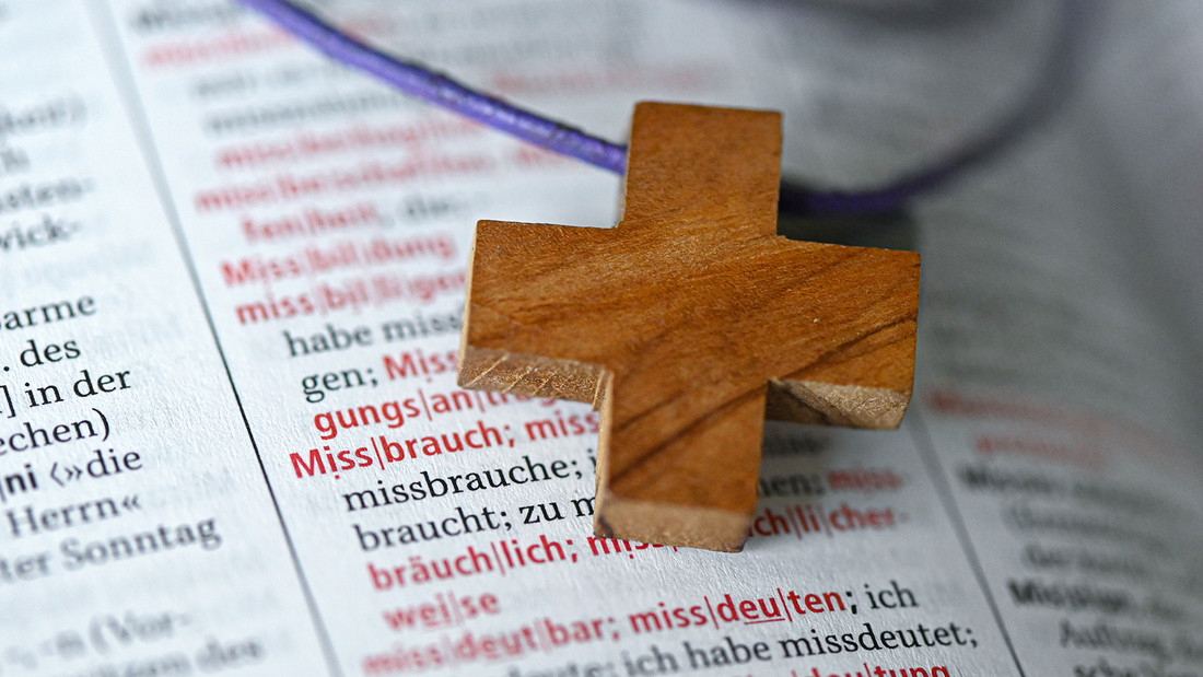Ein Holzkreuz auf dem Wort "Missbrauch"in einem Duden