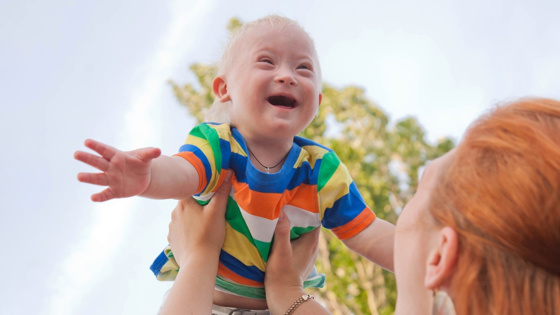 Kind mit Down-Syndrom wird lachend hochgehoben