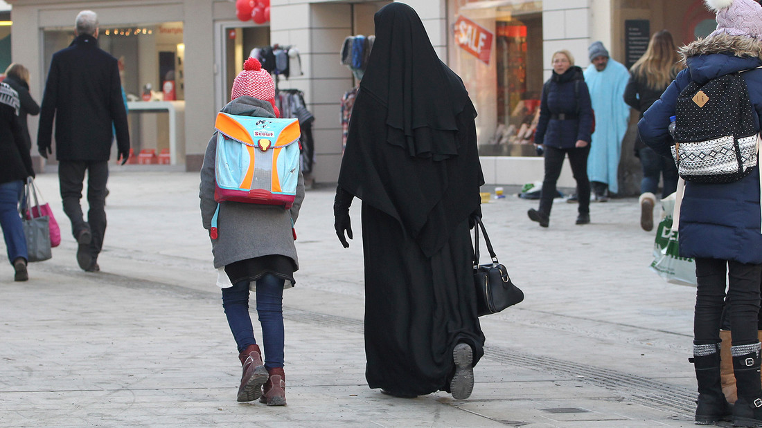 e Frau mit Tschador geht in Begleitung eines Schulkindes