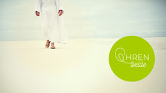Mann läuft im Wüstensand mit weißer Kutte und Sandalen