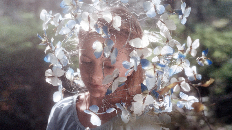 Ein Mädchen mit einem Kopfschmuck aus Schmetterlingen steht im Wald. 