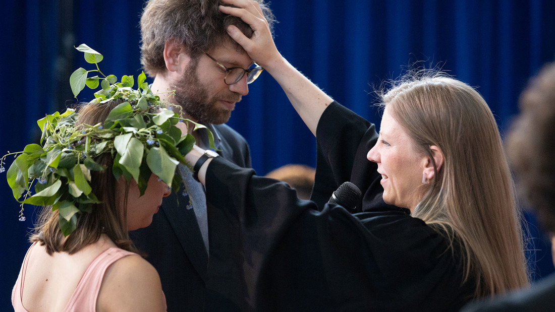 Ein Hochzeitspaar steht vor einer Pastorin, die ihnen den Segen erteilt.