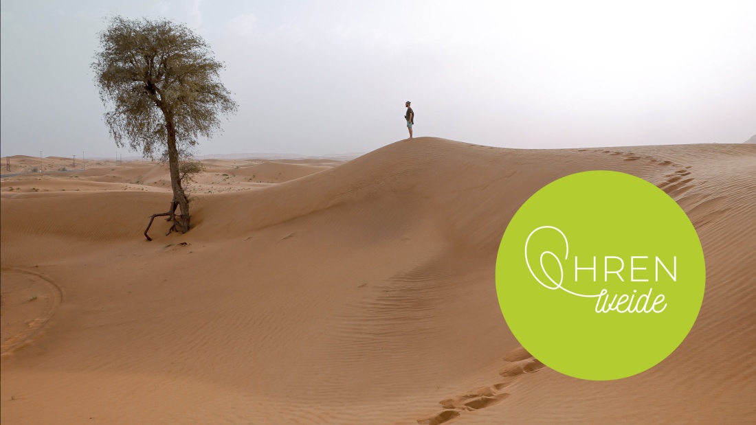 Mann steht in Wüste vor einem grünen Baum
