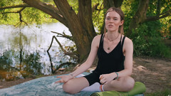 Eine junge Frau sitzt mit Sportkleidung am See.