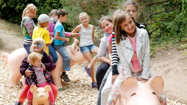 Eine Gruppe von Kindern spielt auf Schweinchen-Figuren.