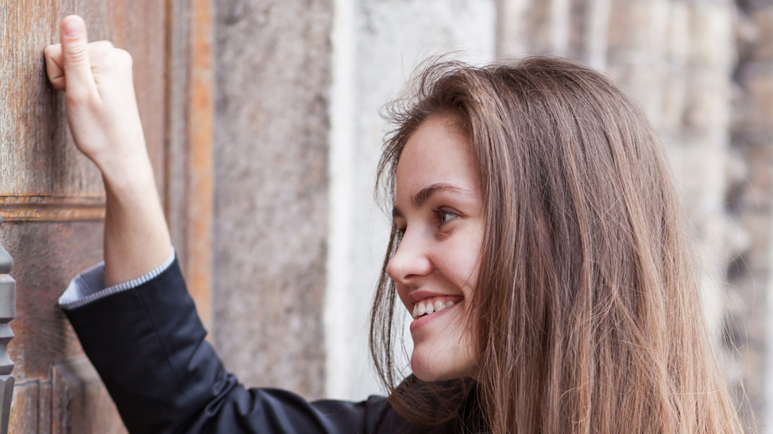 Eine junge Frau klopft lächelnd an eine Kirchentür