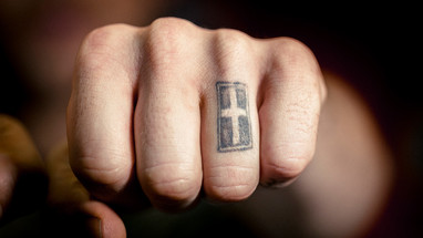 Faust mit einem Kreuz als Tattoo auf einem Finger