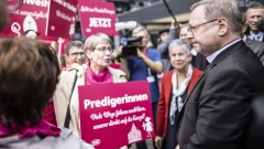 Bischof Bätzing, Vorsitzender der katholischen Bischofskonferenz, steht gegenüber von katholischen Frauen, die Protestschilder hochhalten. 