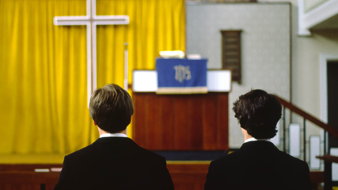Rücken zweier Männer, die vor einem Altar in einer Kirche knien.