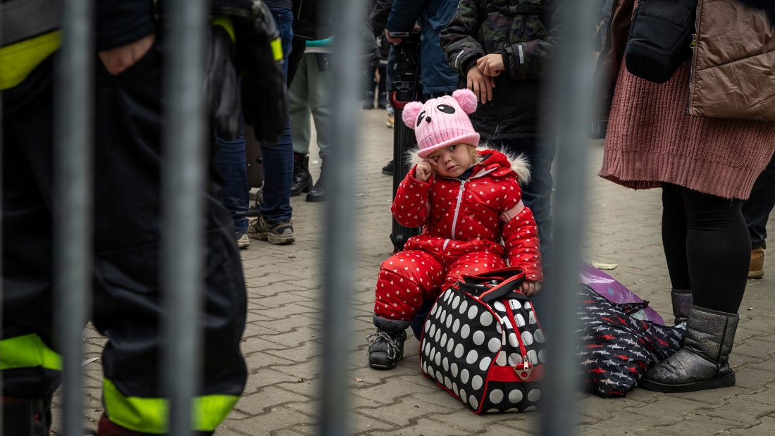 Flüchtlingskind sitzt weinend auf Reisetasche an Grenzübergang