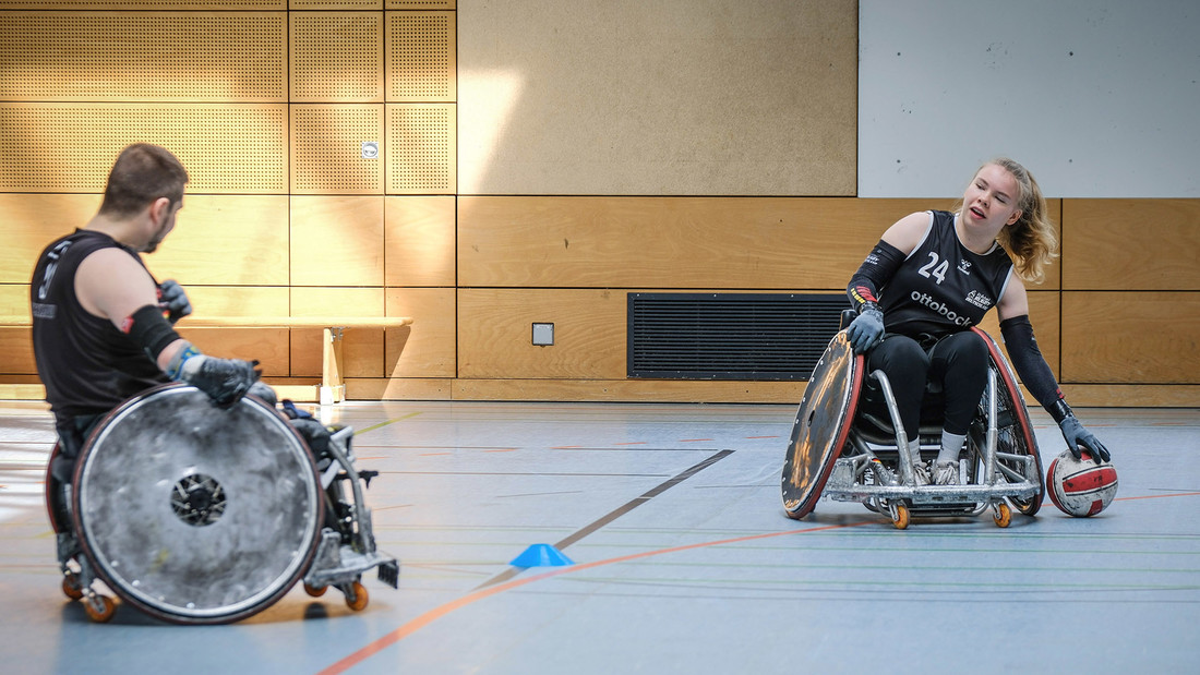 Ein Rollstuhlfahrer und eine Rollstuhlfahrerin trainieren in einer Sporthalle Rollstuhlrugby.