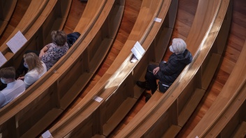 Gläubige sitzen mit Abstand und mit Masken auf Kirchenbänken