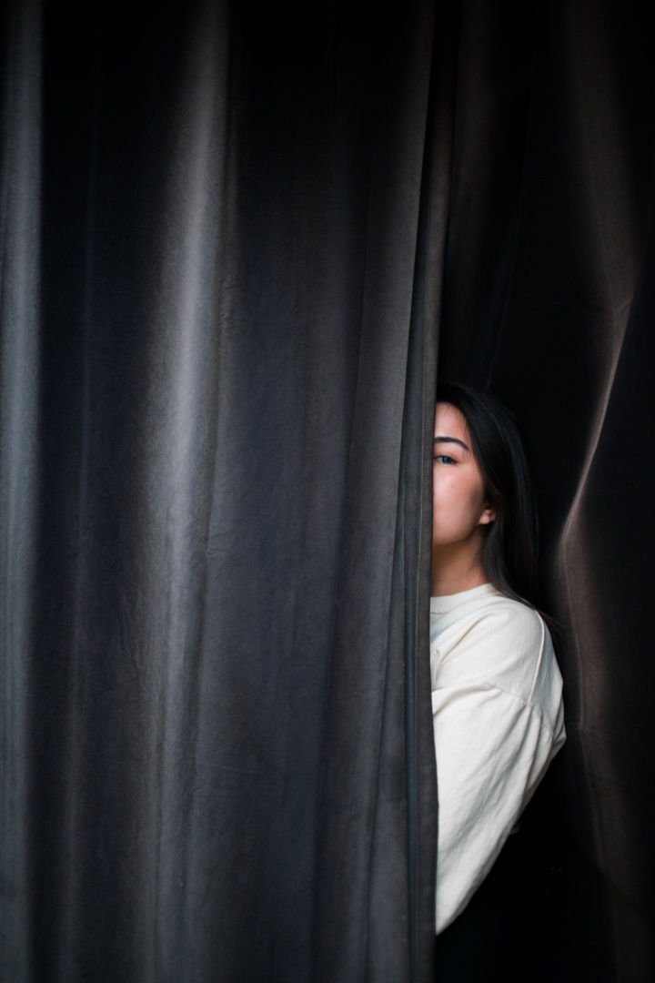 Eine Frau versteckt sich zur Hälte hinter einem Vorhang.