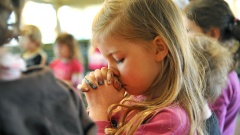 Mädchen in pinkem Pulli betet mit geschlossenen Augen