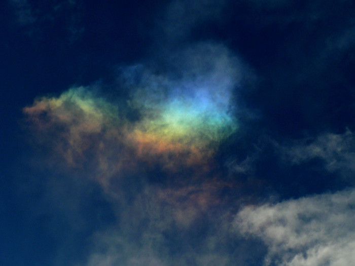 Dunkelblauer Himmel mit weißen Wolken und einemzarten Regenbogen