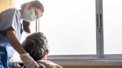 Krankenschwester mit Maske schiebt Senior in Rollstuhl