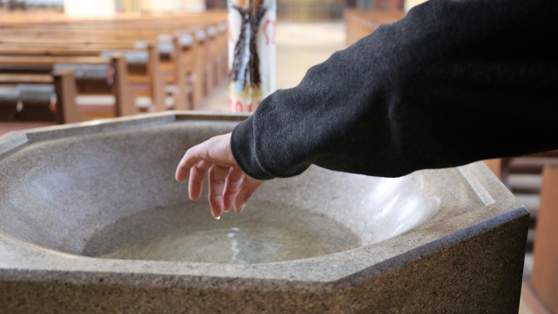 Hand taucht in Weihwasserbecken