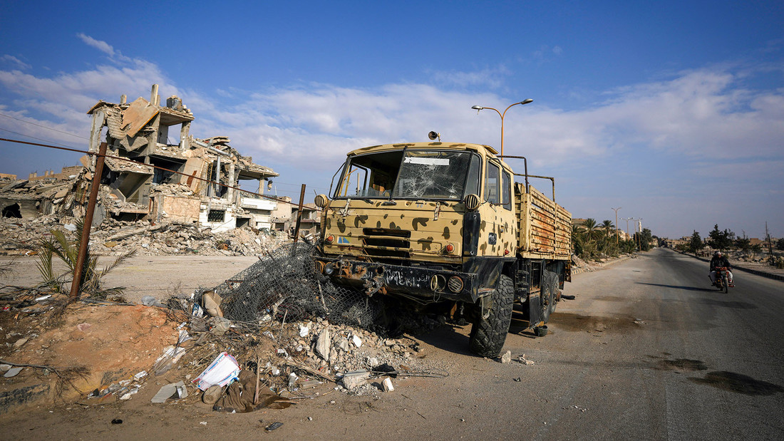 In der syrischen Stadt Palmyra fährt ein Mann auf einem Motorrad an einem zerstörten Militärlastwagen der gestürzten Assad-Regierung vorbei.