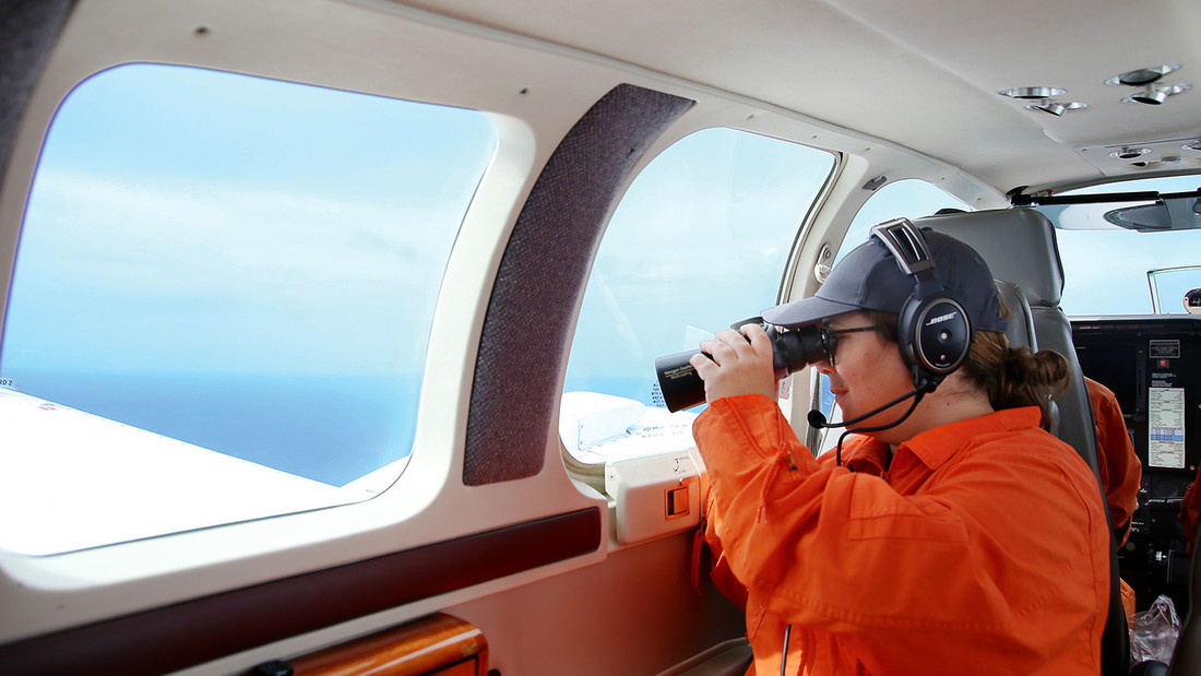 Stefanie Sargnagel sitzt in einem Flugzeug und schaut durch ein Fernglas.