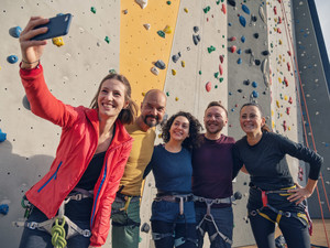 Eine Gruppe junge Menschen fotografieren sich vor einer Boulderwand 