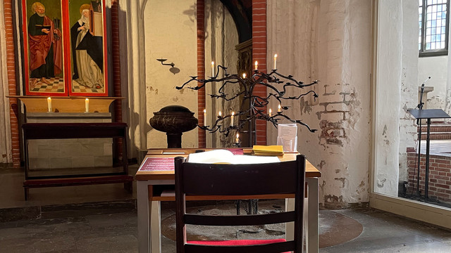 Tisch mit Kerzen, Umschlägen und Schreibpapier in einer Kirche.