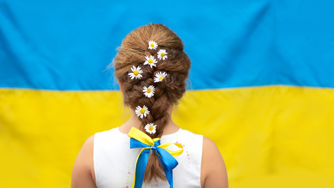 Mädchen mit Gänseblümchen im Haar vor ukrainischer Flagge